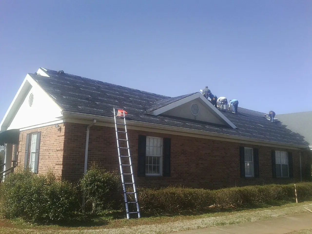Crew tearing shingles off a brick ranch roof with a ladder set — Metal Roof Repair work by our crew in Sadsburyville