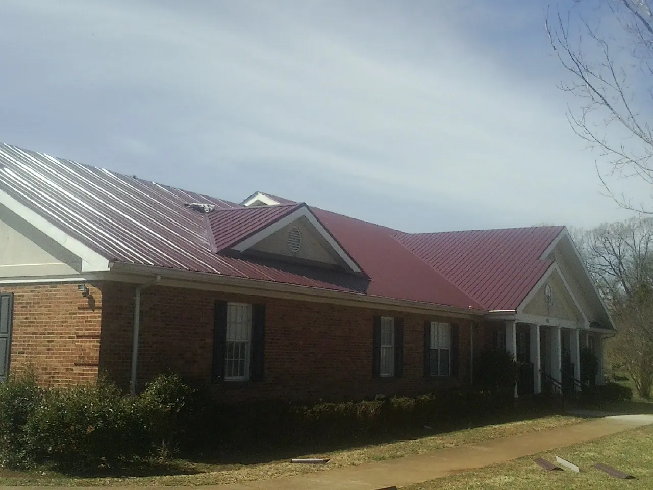 Red metal roof with gabled entries on a long brick building, from a Hail Damage Roof Repair job in Sadsburyville
