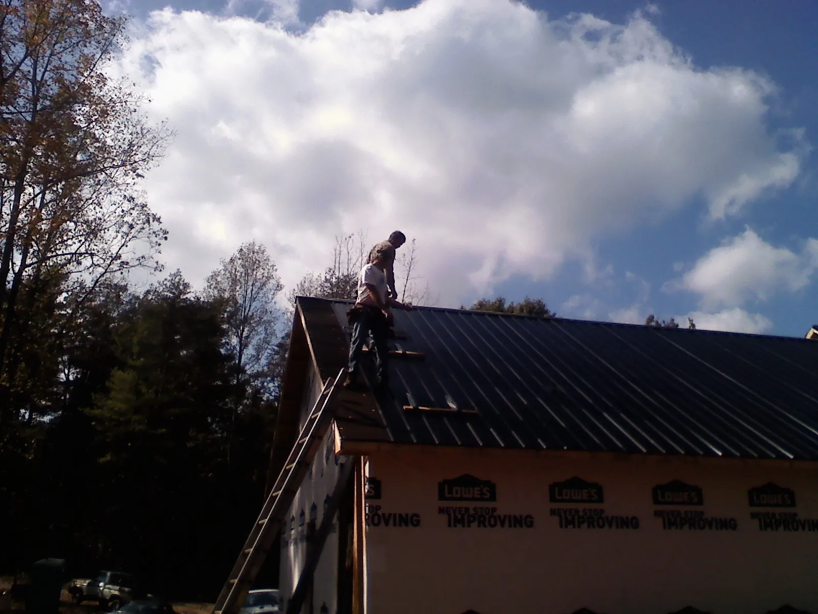 Roofer fastening dark metal panels high against a cloudy sky, from a Roof Inspection job in Sadsburyville