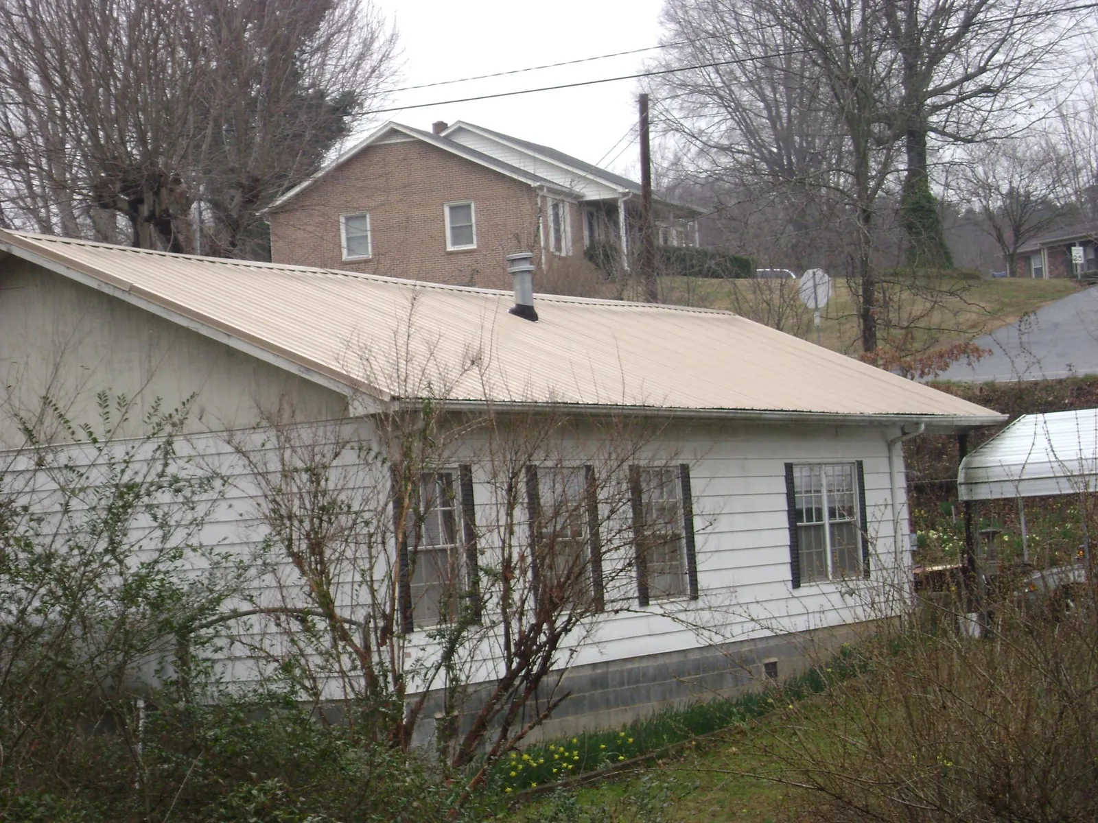 Tan metal roof on a white sided house set into a hillside — Commercial Roofing by Roofing Brothers in Sadsburyville